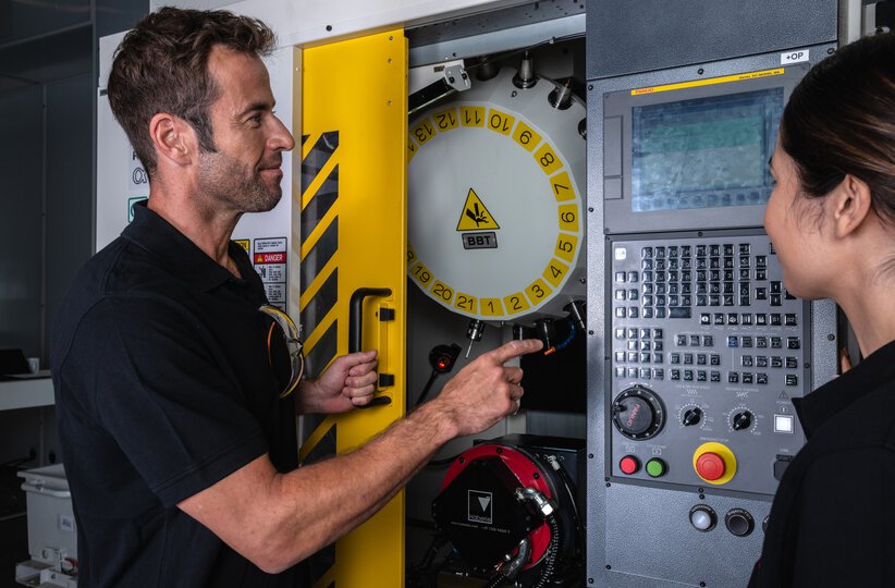 Service / maintenance photo with person. Woman and man in front of a ROBODRILL with the door open. Landscape. High resolution.