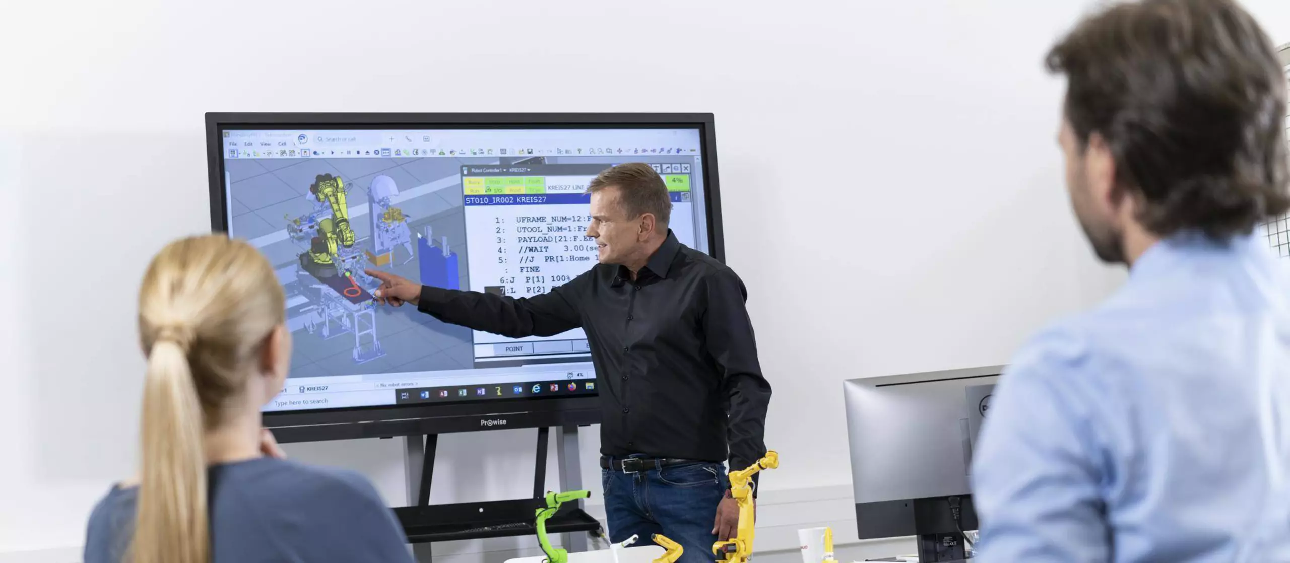 Image showing FANUC Academy trainer explaining two partipants the ROBOGUIDE Handling Pro software.