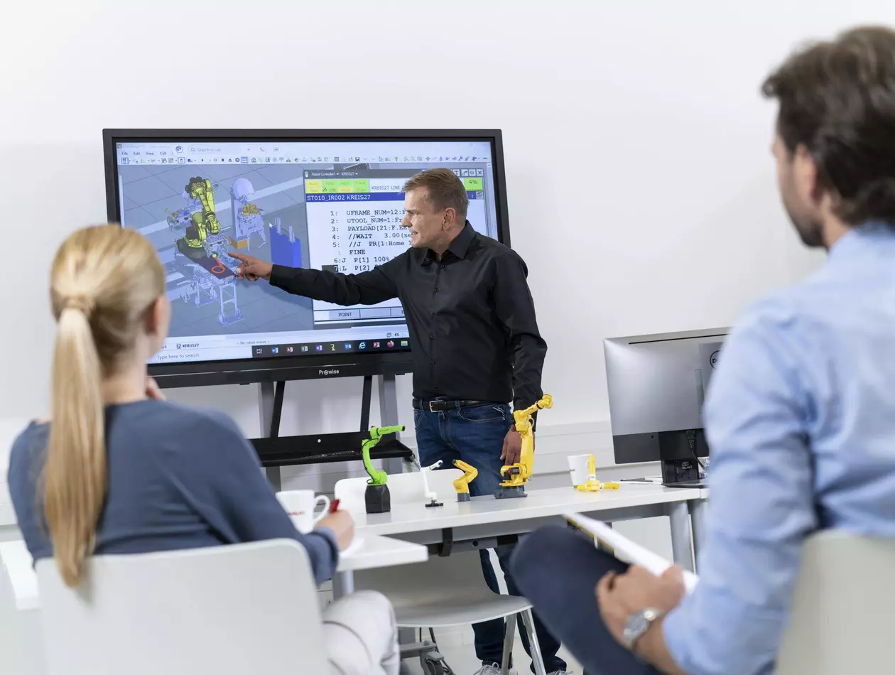 Image showing FANUC Academy trainer explaining two partipants the ROBOGUIDE Handling Pro software.