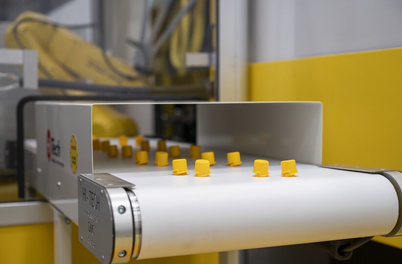 Virtual show 2021. Detail image of ROBOSHOT plastic workpieces coming out of a conveyer belt.